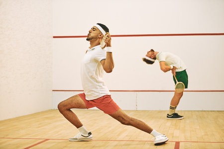 Warming up prepares you physically and mentally for the game. two young men stretching before playing a game of squash.の写真素材