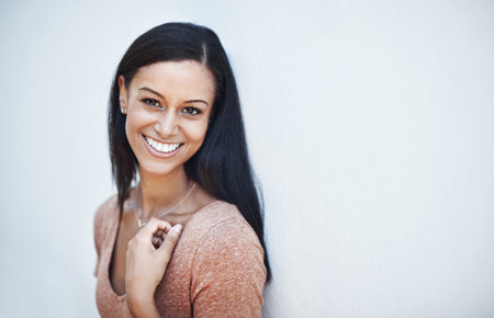 What a stunningly beautiful smile. a happy and attractive young woman leaning against a wall outside.の写真素材