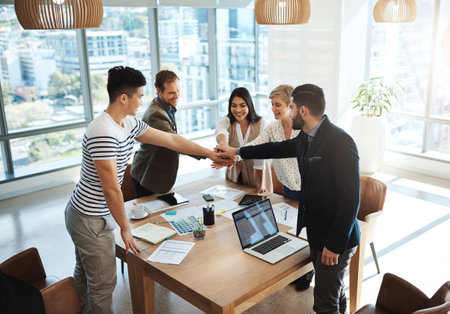 Together we can achieve greatness. a diverse group of businesspeople joining their hands in a huddle in an office.の写真素材