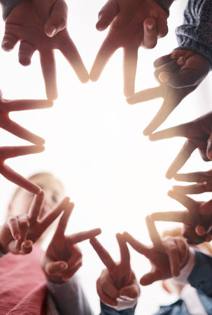 Lets keep it real. Low angle shot of a group of cheerful elementary school kids forming a huddle with their hands and showing a hand sign.の写真素材