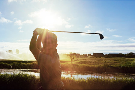 Swinging into action. a man practicing his swing on the golf course.の写真素材