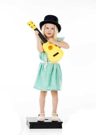 Shes a mini musician. Studio shot of a cute little girl playing with her toy guitar against a white background.の写真素材