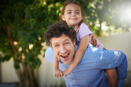 Family life is never dull around here. Portrait of a father giving his daughter a piggyback ride outside.の写真素材