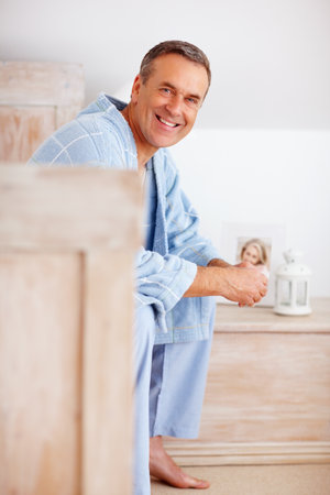 Smiling mature man in bathrobe sitting on bed. Portrait of a smiling mature man in bathrobe sitting on bed.の写真素材