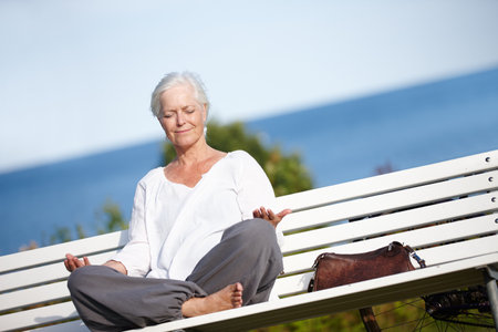 Meditating with the sounds of nature. a mature woman meditating on a park bench.の写真素材