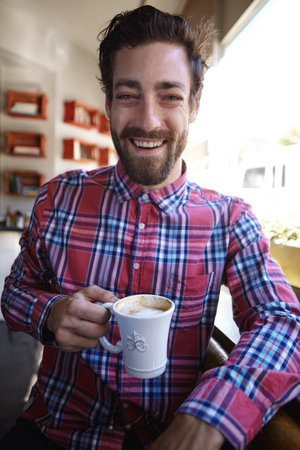 With enough coffee, anything is possible. a young man drinking a cup of coffee in a coffee shop.の写真素材