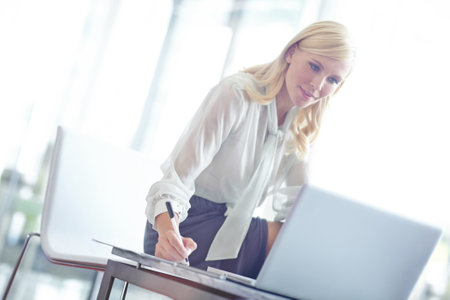 Showing ambition. a beautiful business woman sitting on her desk and writing notes from her laptop.の写真素材