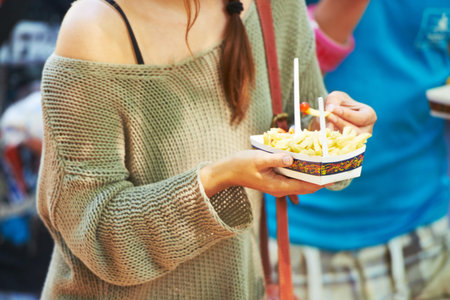 Festival food. a young woman eating french fries at an outdoor festival.