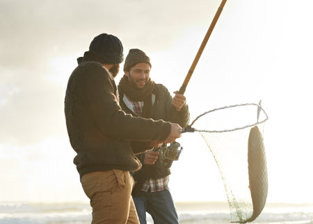 Catching the big one. two young men fishing at the beach.の写真素材