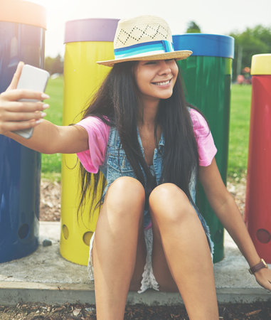 Putting on her best selfie smile. an attractive young woman taking selfies while spending a day in the park.の写真素材