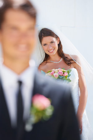 She stands behind him. A stunning bride smiling happily while her husband-to-be stands blurred in the foreground.の写真素材
