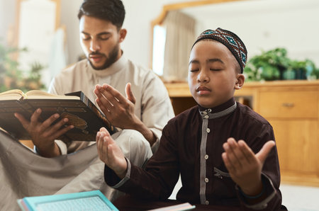 Your prayers for your children are the greatest legacy. a young muslim man and his son reading in the lounge at home.の写真素材