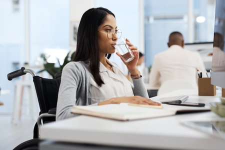 Staying hydrated through the workday. an attractive young businesswoman drinking water while working at her desk in the office.の写真素材
