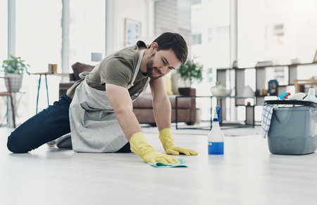 Getting rid of dirt and grime take some elbow grease. a young man wiping the floor at home.の写真素材