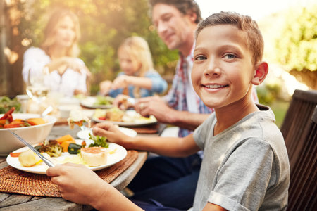 Family for always and forever. Portrait of a happy little boy enjoying an outdoor lunch with his family.の写真素材