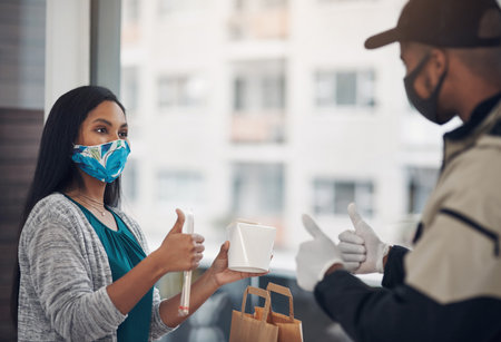 Self isolating Suppers on us. a masked young man showing thumbs up while delivery takeout to a customer at home.の写真素材