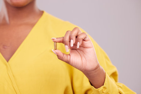 Pharmaceutical, hand and woman with a pill in a studio for healthcare, wellness or recovery medication. Medical, medicine and closeup of female person with tablet capsule isolated by gray background.の写真素材