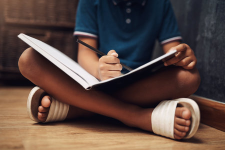 Writing is a great way to share your thoughts. an unrecognizable boy writing in a book at home.の写真素材
