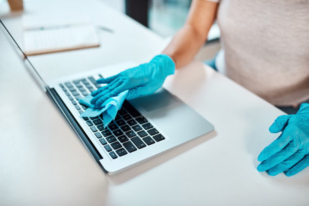 Disinfect high-touched surfaces daily. Closeup shot of an unrecognisable businesswoman cleaning a laptop in an office.の写真素材