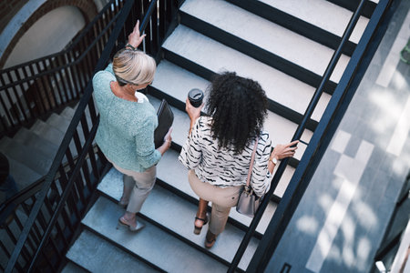 On the go and on the grow. two businesswomen having a discussion while walking up the stairs in a modern workplace.の写真素材
