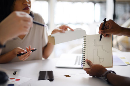Building something this big requires lots of brainpower. Closeup shot of a group of unrecognisable businesspeople analysing blueprints together in an office.の写真素材