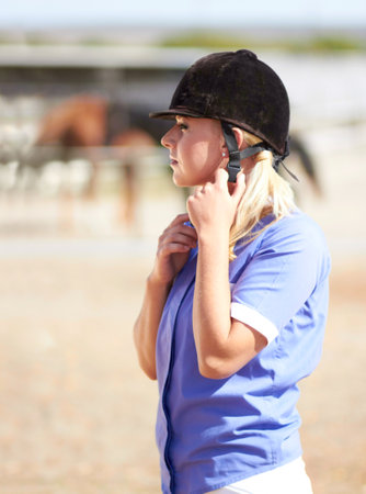 Woman prepare, horse jockey and helmet of young athlete on equestrian training ground for show and race. Outdoor, female person and equipment fixing on animal farm for dressage with rider and horsesの写真素材