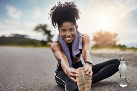 Stretching every joint and muscle. Portrait of a sporty young woman stretching her legs while exercising outdoors.の写真素材