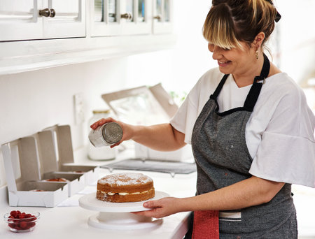 Earn while doing what you enjoy. a woman decorating a cake in her kitchen.の写真素材