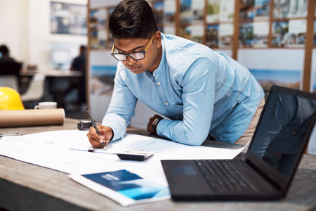 Uplifting designs that uplift a city. a young architect drawing up a building plan in a modern office.の写真素材