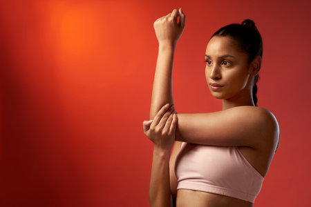 Push your mind so you can push your body too. Studio shot of a sporty young woman stretching her arms against a red background.の写真素材