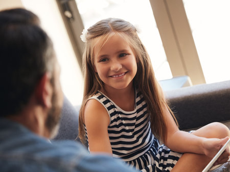 Want a turn on the tablet, dad. an adorable little girl using a digital tablet with her father on the sofa at home.の写真素材