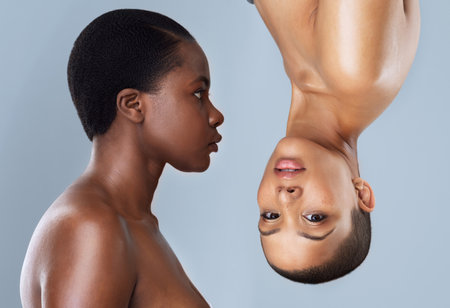 You spin me upside down. Portrait of two beautiful young women standing close to each other with one upside down against a grey background.の写真素材