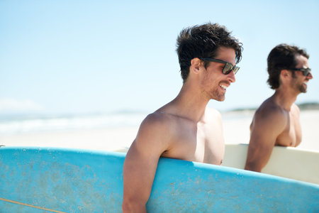 Invigorated after a surf. Two friends walking along the beach while carrying their surfboards.