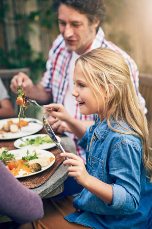 Eat good, feel good. a happy little girl enjoying an outdoor lunch with her family.の写真素材