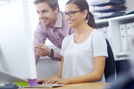 Now youre getting the hang of it. a handsome young man helping a female coworker on her computer.