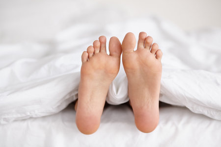 Wiggling toes of wakefulness. a pair of womans feet poking out from under the sheets of a bed.の写真素材