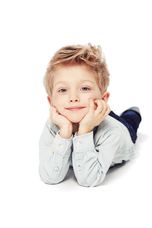 Portrait, smile and boy lying down, relax and cheerful kid isolated against white studio background. Face, male child or young person with happiness, casual and chilling with joy, happy and confidentの写真素材