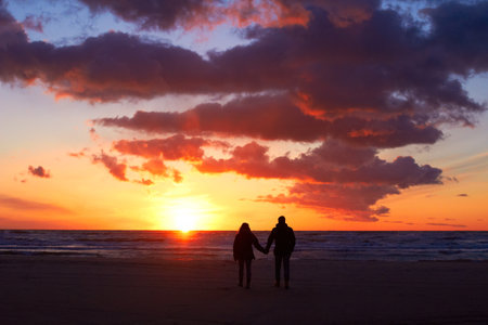Silhouette, couple holding hands at sunset and on beach walking together. Love or care, holiday or vacation and shadows of people on the seashore for embrace for romance date or honeymoon outdoorの写真素材