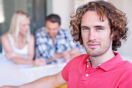 His talents are well known to his colleagues. A young man with curly hair sitting in the boardroom with his peers.の写真素材
