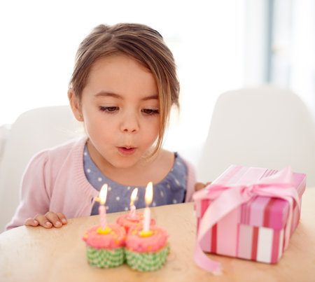Its my birthday. a young girl blowing out the candles on her birthday cupcakes.の写真素材