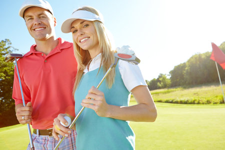 Spending a day on the green. Attractive young couple with their golf clubs and balls on the green.の写真素材