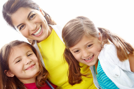 Two girls and their mother. Portrairt of a young mother hugging her daughters affectionately against a bright background.の写真素材