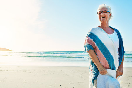 The beach always makes her smile. a senior woman visiting the beach on a summers day.の写真素材