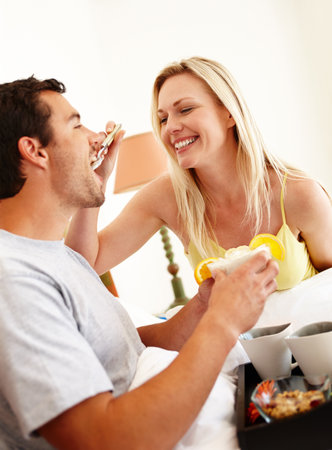 Mmm, its delicious. A happy young couple enjoying breakfast together in bed at home.の写真素材