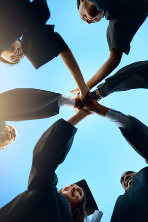 The future belongs to us. Low angle shot of a group of young students joining their hands together on graduation day.の写真素材