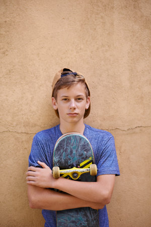 Skateboarding close to his heart. Portrait of a teenage boy holding his skateboard while standing...