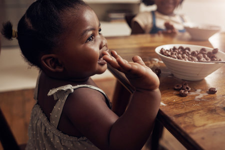 Everyone loves a chocolatey breakfast. an adorable baby girl eating cereal at home with her elder...