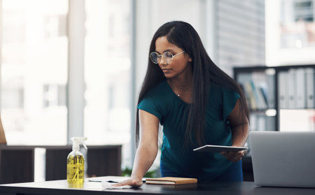 Keeping things sanitary around her workspace. a young businesswoman cleaning a workspace in an office.の写真素材