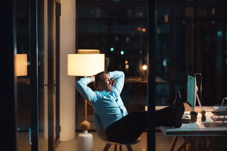 He aced that late night project. a mature businessman relaxing at his desk during a late night at work.の写真素材