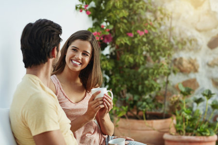 Taking a coffee break together. a happy young couple having coffee together on a bench outside.の写真素材